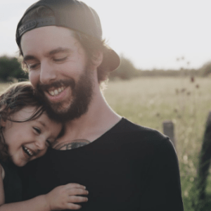 A joyful father holds his smiling daughter in a sunlit field, showcasing their close bond and a serene summer day.